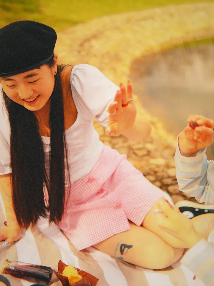 A woman in a pink skirt at a lakeside picnic — 2010 · Square Feed